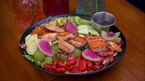 dolly in shot of a plate with a healthy snack with grilled salmon tomatoes grapes cucumbers radish and other vegetables