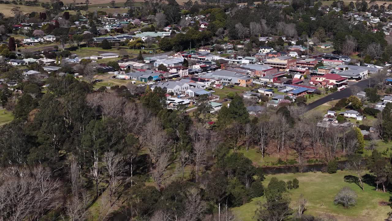 Drone ascends over Dorrigo, revealing rural town, houses, shops, and green landscape in daylight