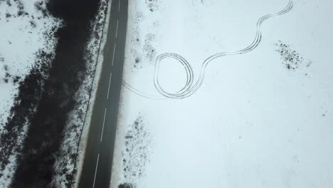 a car driving past mysterious tire tracks in snow, chilly winter landscape, drone footage, eerie feeling scene