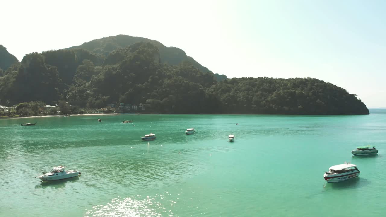 Boats undisturbed resting above emerald green sea in Phi Phi Don Island Paradise in Thailand - Aerial slide low Fly-over shot