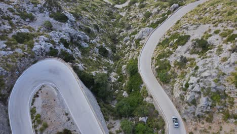 drone view of a single car driving down a windy mountain road at sa calobra, mallorca, spain