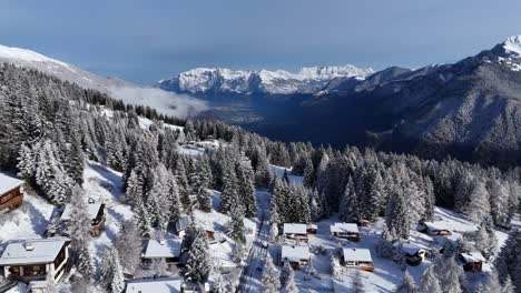 tomada amplia del dron que muestra un pequeño pueblo suizo en una montaña nevada con una cordillera helada en el fondo durante un día soleado - chur, suiza