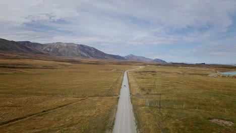 un vehículo que navega por un camino de tierra accidentado rodeado de paisajes rurales áridos con montañas majestuosas y un lago tranquilo en la distancia, bañado por la cálida luz del sol