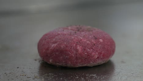 Close-up-of-a-raw-burger-patty-being-placed-on-a-restaurant-griddle-to-cook