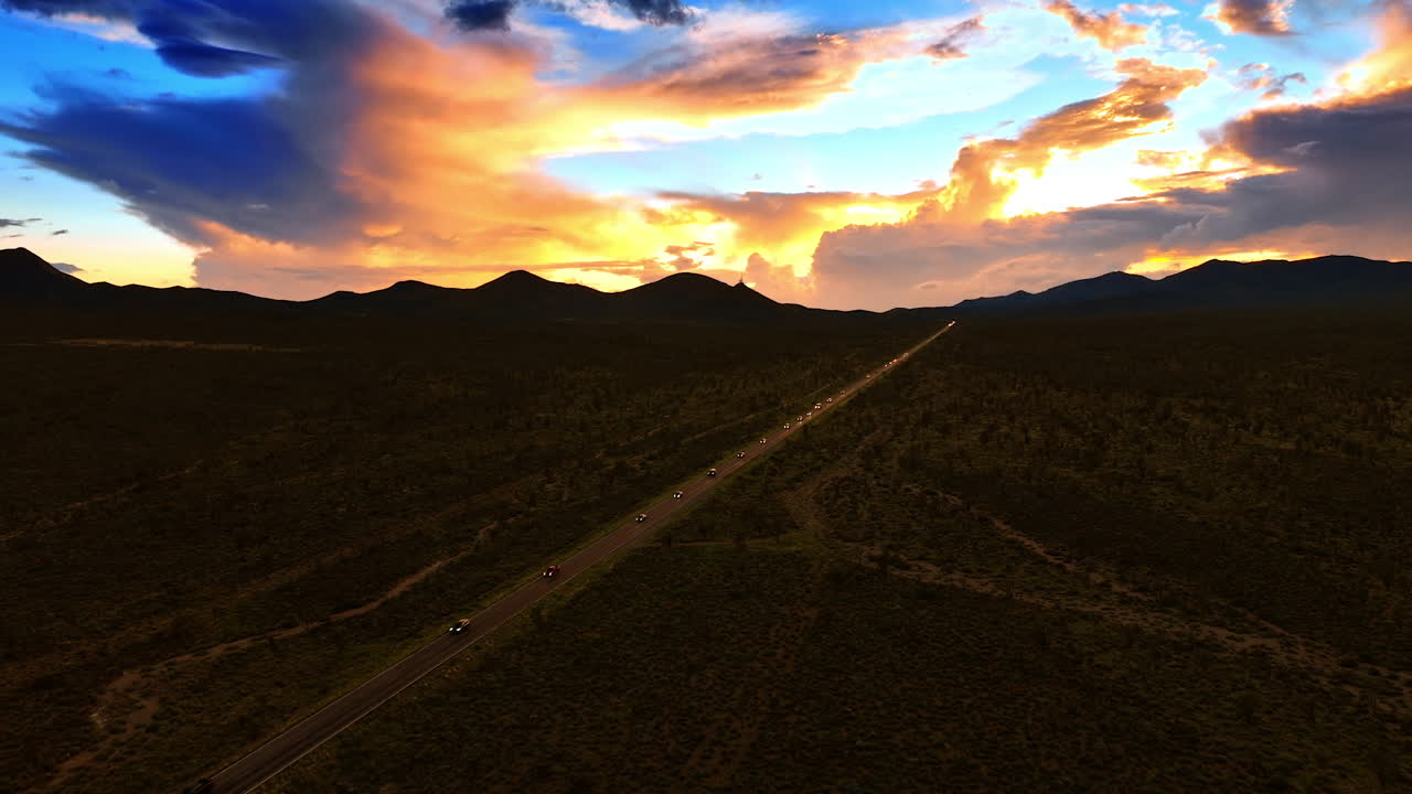 Cars run with headlights on by the highway in Death Valley after sunset. Beautiful colorful clouds in the sky over the scenery. Aerial view.