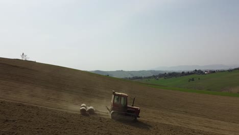 Aerial-view-of-red-crawler-tractor-pulling-a-rolling-system-for-land-plowing-and-seeding-preparation-in-remote-Italian-countryside