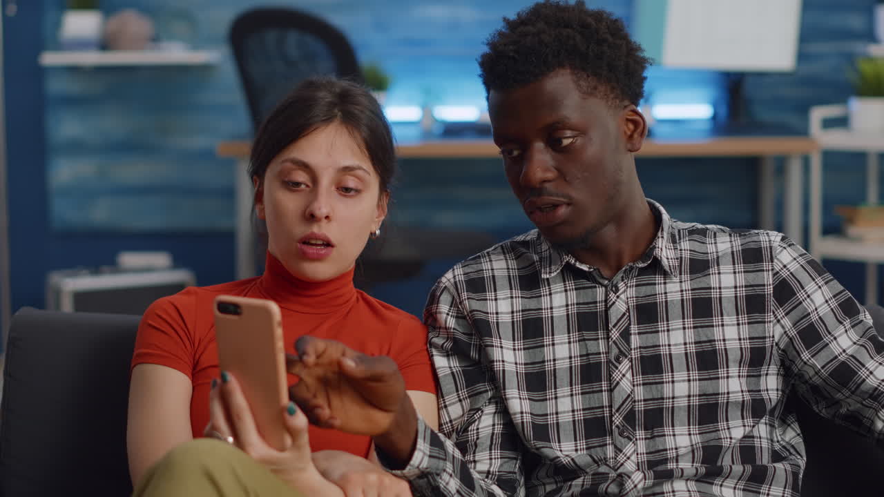 Modern interracial couple using smartphone in living room