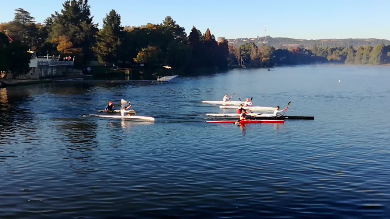 Group of kayakers rowing around a dam early one autumn morning. Still some mist over the water and trees are beginning to go yellow.  Emmarentia dam, Johannesburg Botanical Gardens, South Africa