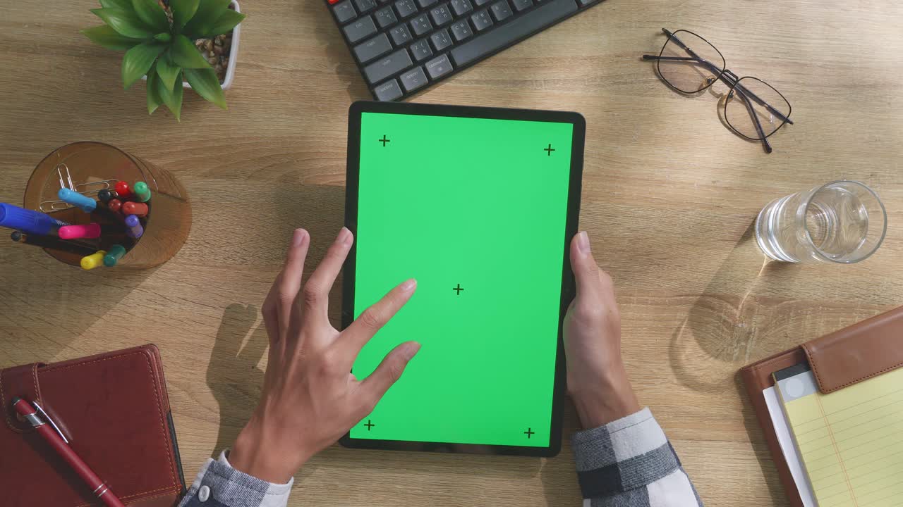 vista de arriba hacia abajo de una computadora portátil con pantalla verde simulada pantalla chromakey en un escritorio de oficina de madera al lado de la libreta con bolígrafos, gafas y un vaso de agua.
