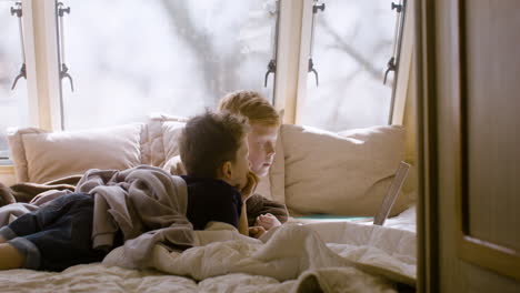 Two-little-brothers-lying-on-bed-in-a-campervan-and-watching-something-on-laptop-computer