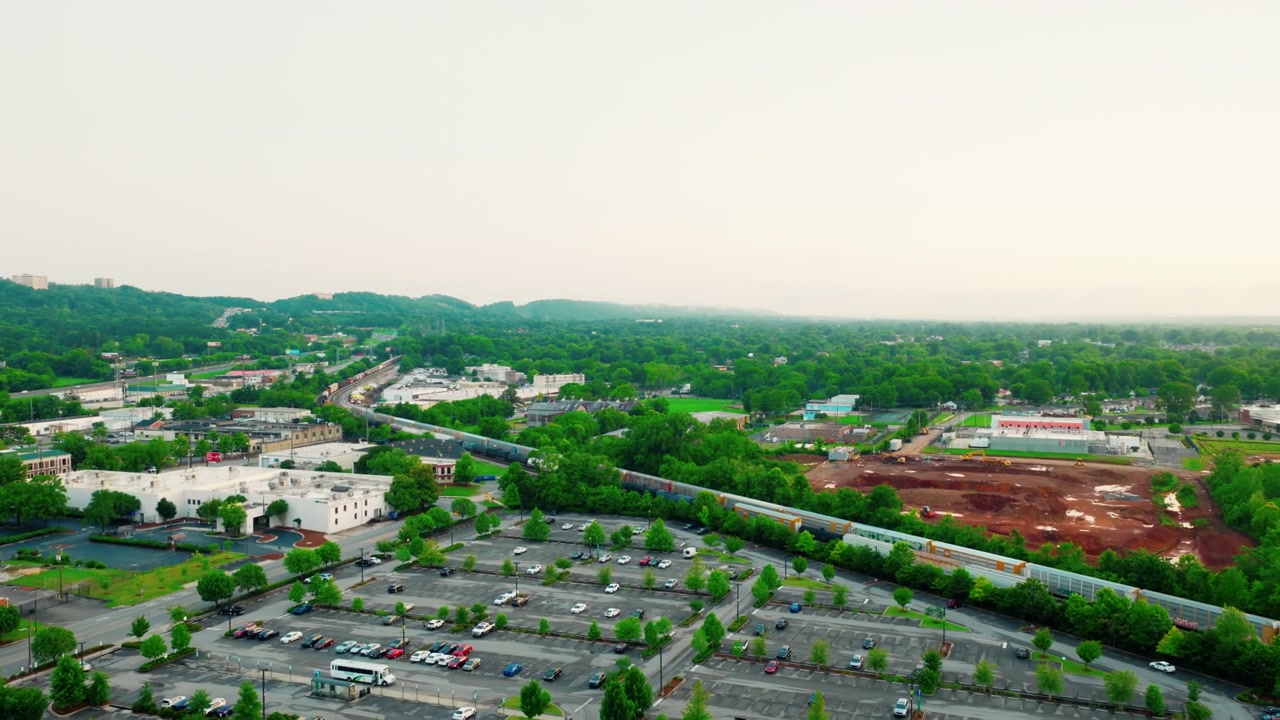 Lungo treno merci che trasporta carico attraverso un'area suburbana sviluppata di Birmingham, Alabama, con parcheggi e vegetazione
