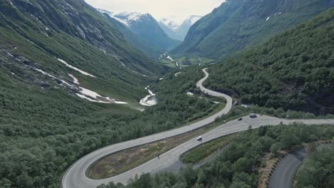 winding mountain valley road with driving vehicles in stryn, norway, aerial fpv view