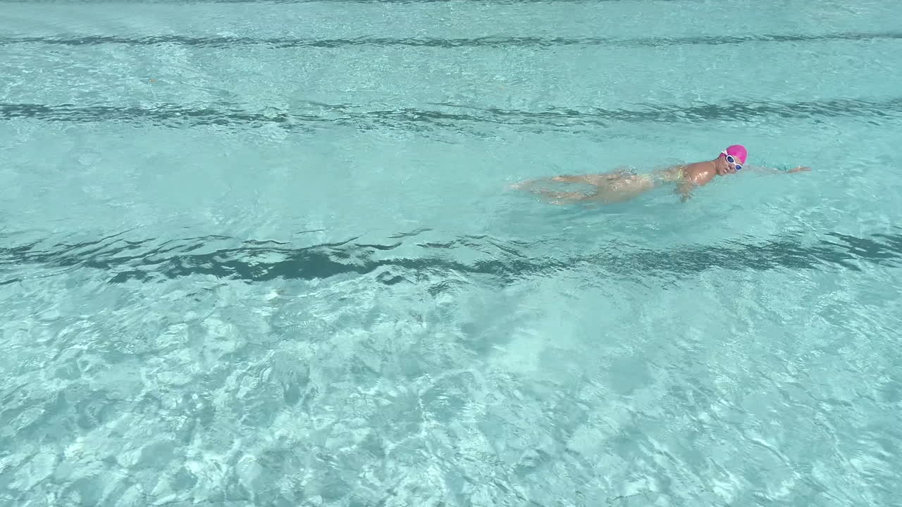 女子水泳選手がトライアスロンのトレーニング計画の一環としてフリースタイル ストロークを使用して屋外プールでラップを泳いでいる映像
