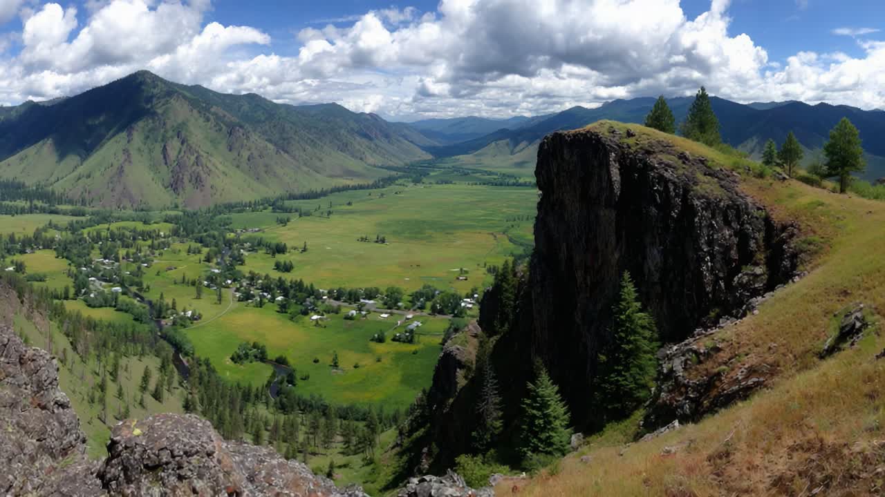 Stunning Panoramic View of Lush Green Valley Surrounded by Majestic Mountains and Rocky Outcrops Under a Bright Blue Sky with Fluffy White Clouds
