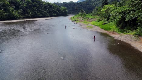 Aerial-dolly-over-fishermen-crossing-wide-tropical-river-in-lush-green-valley