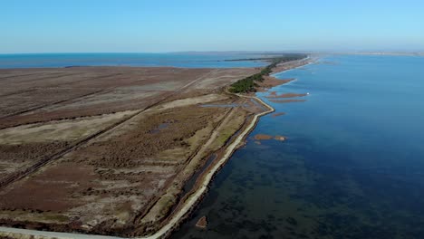 Laguna-Poco-Profunda-Con-Aguas-Tranquilas-Y-Claras-Bordeada-Por-Una-Estrecha-Franja-Terrestre-Desde-El-Mar-Azul-Junto-A-Marismas,-Vista-Aérea