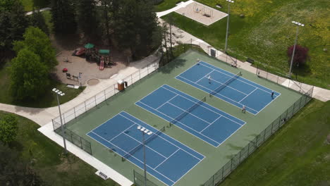 Una-Toma-Aérea-De-Canchas-De-Tenis-Duras,-Donde-Los-Jugadores-Juegan-Dobles