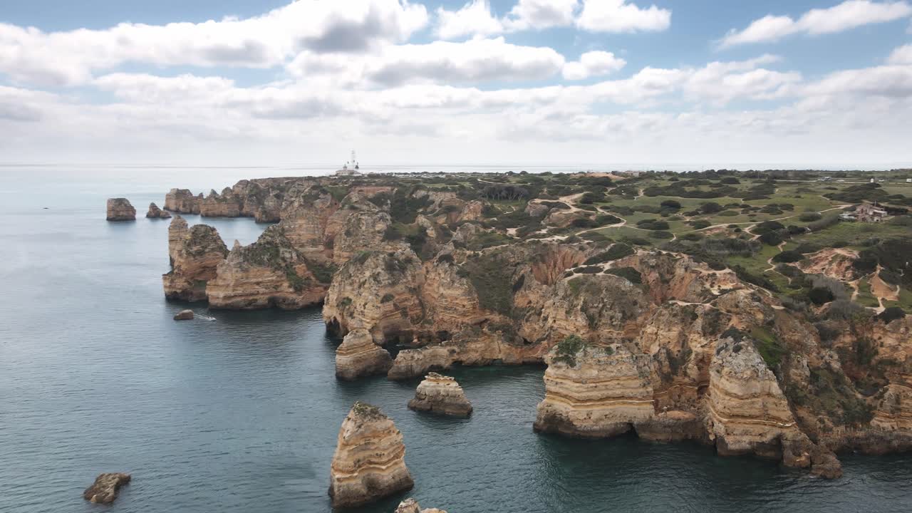Aerial drone glides right, revealing dramatic limestone cliffs and rugged coastline in Algarve near Lagos
