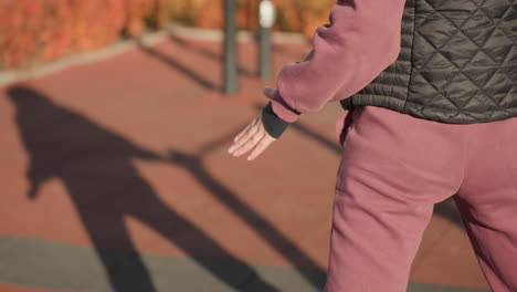 shadow silhouette of fitness devotee swaying in side lunge under bright sun on outdoor gym court, metal bars casting long shapes across rubber tiles, autumn shrubs glowing beside paved promenade