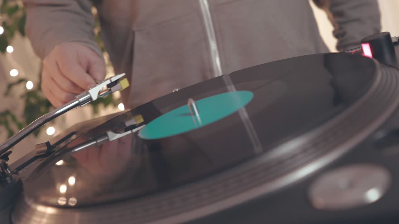 фрагмент вращающейся виниловой пластинки на диджейском пластинщике на фоне ярких партийных огней. диджей подходит к музыкальному проигрывателю и ставит стилус с иглой. боковой вид