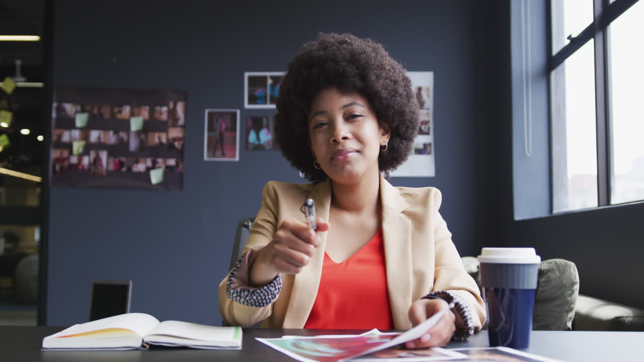 Biracial businesswoman sitting having a video chat going through paperwork in a modern office