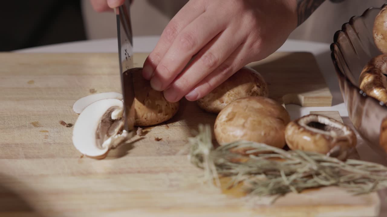 Woman's Hand Slicing Portobello Mushrooms On Wooden Chopping Board With Rosemary