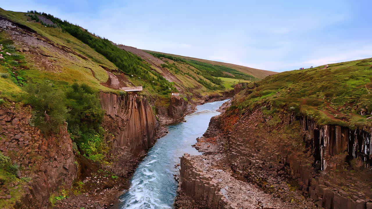 Columnar rocks tower above the narrow river. Some mountain tops have the observation decks on tops. Iceland scenery.