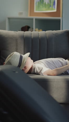 little girl with braided hair pulls suitcase around sofa with lying toddler brother in living room. funny naughty children ready for summer travel