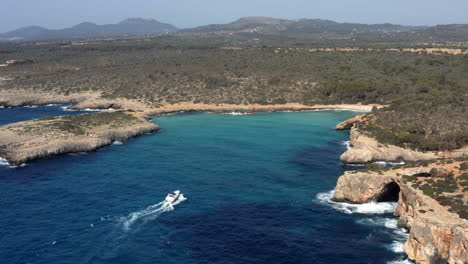 yacht sailing along rock cliffs into beach lagoon of cala varques