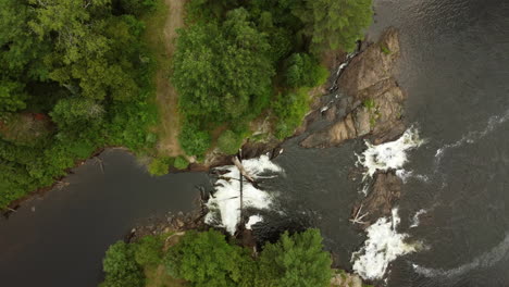 vista de pájaro de una cascada que se sumerge en las profundidades entre la vegetación verde sobre rocas cubiertas de vegetación