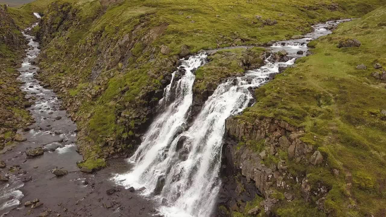 dolly aéreo en cascadas de glymur y río que fluye por un acantilado rocoso rodeado de verdes tierras altas durante el día, islandia