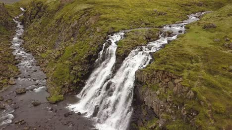 Aerial-dolly-in-of-Glymur-waterfalls-and-river-streaming-down-rocky-cliff-surrounded-by-verdant-highlands-at-daytime,-Iceland