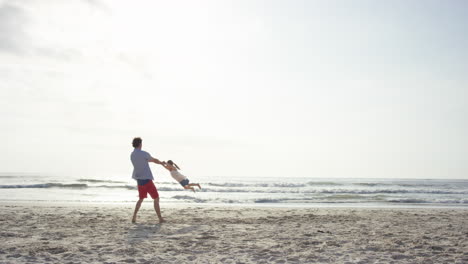 Vater-Schwingt-Tochter-Bei-Sonnenuntergang-Am-Strand-Herum-Und-Hat-Spaß