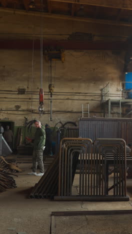 worker pulls goat crane hook walking along plant workshop slow motion. employee in uniform operates with lifting equipment at metalworking factory