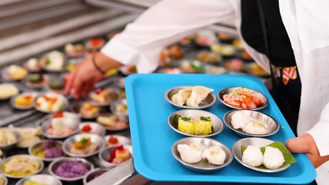 A vendor arranges colorful dim sum on a tray in a bustling Phuket market. Bright lighting enhances the vibrant atmosphere