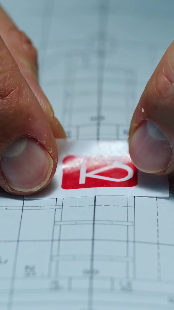 Vertical video: Holding backing, hands aligning, pressing red sticker on drawing to mark centerline