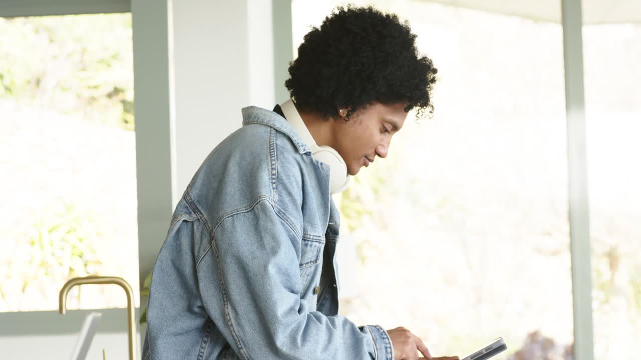 African American man scrolling phone in kitchen then tapping tablet focusing on tasks copy space