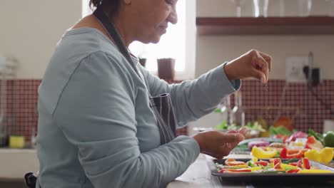 mujer asiática mayor rociando orégano sobre ensalada de verduras en la cocina en casa