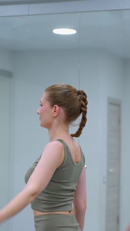mujeres participan en una sesión de entrenamiento, quitando las manos de la cabeza mientras realizan un estiramiento de la columna vertebral, un gran espejo refleja el entorno del gimnasio
