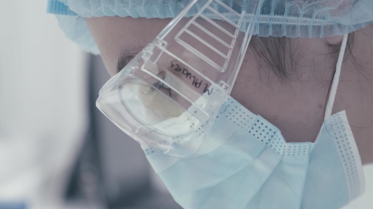 Female scientist wearing a mask and glasses checking an object that has been observed in a modern research laboratory, focus on face