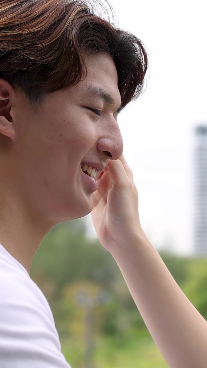 ภาพโคลสอัพด้านข้างของชายชาวเอเชียยิ้มแย้มที่ถูกสัมผัสอย่างอ่อนโยนโดยคู่รักของเขาในที่กลางแจ้ง