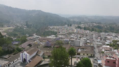 Imágenes-Aéreas-Panorámicas-De-Izquierda-A-Derecha-En-La-Ciudad-De-Chichicastenango-Con-Una-Iglesia-En-Primer-Plano-Y-El-Colorido-Cementerio-Al-Fondo