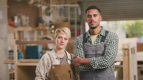 portrait of serious male and female apprentices working as carpenters in furniture workshop