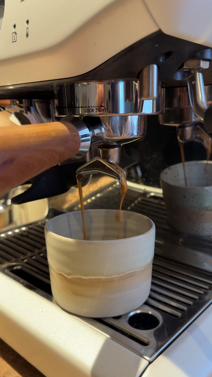 Close-up of rich espresso extraction flowing from a professional coffee machine into a ceramic cup. Dark crema forms as liquid streams evenly, highlighting barista technique and café atmosphere.