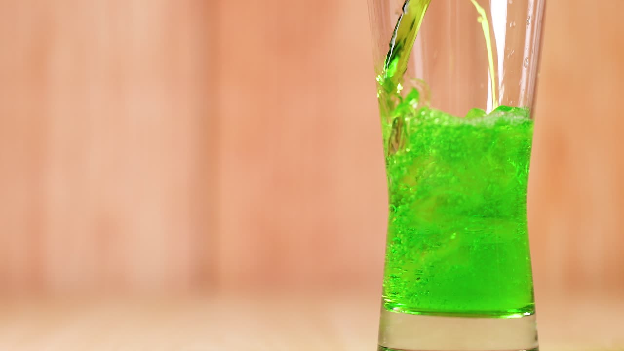 зеленая жидкость постепенно заполняет прозрачный стакан