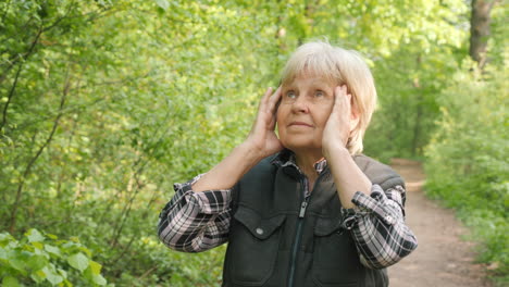 elderly woman experiencing a headache in a forest