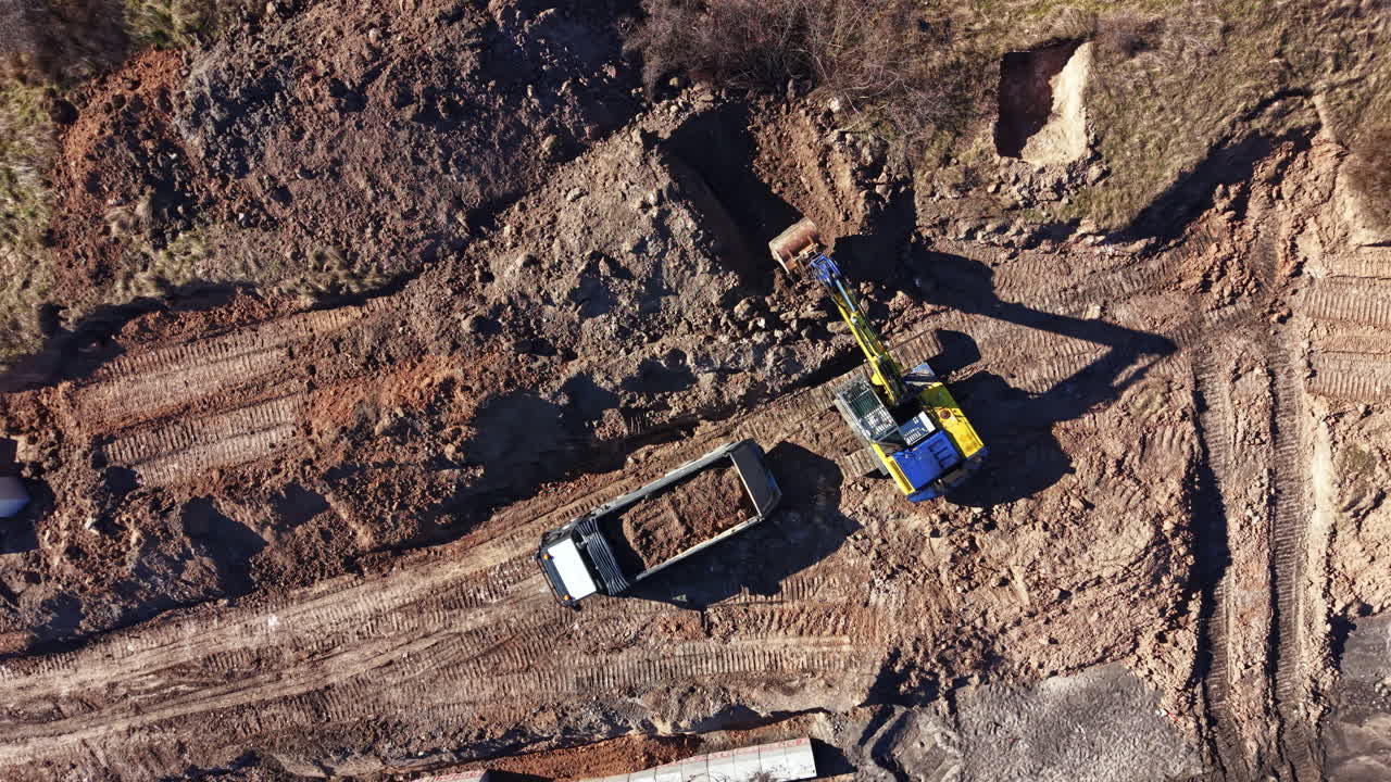 Construction work takes place on a large site with heavy machinery moving and digging in an open area during daytime