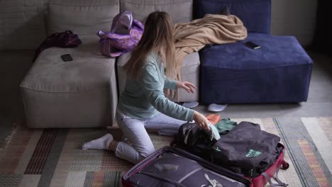 una mujer en una sala de estar pone cosas en una maleta, en cámara lenta