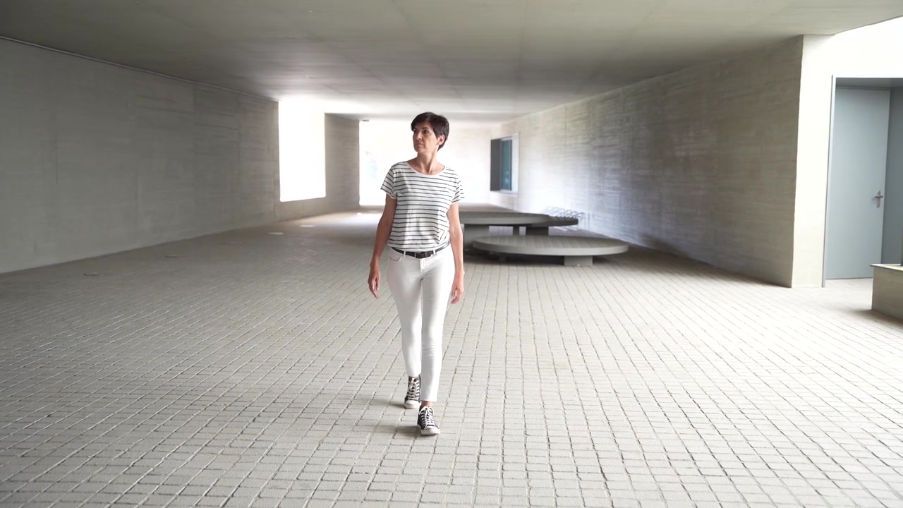 Una giovane donna che cammina elegantemente attraverso uno spazio architettonico contemporaneo, mettendo in mostra il suo stile.