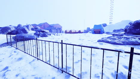 snow covered landscape featuring a fence near rustic buildings in winter